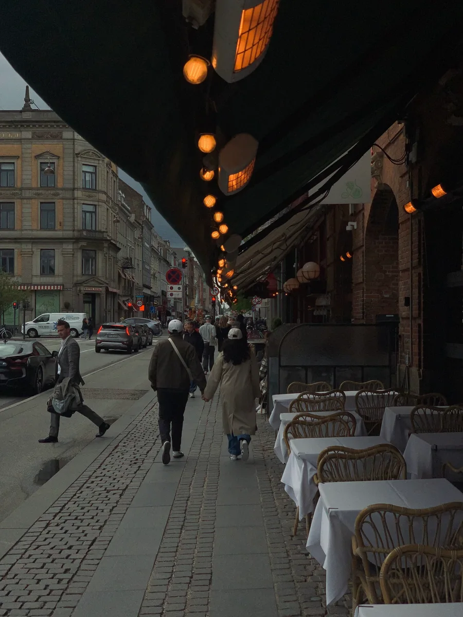 People walking past outdoor restaurant tables beneath an awning