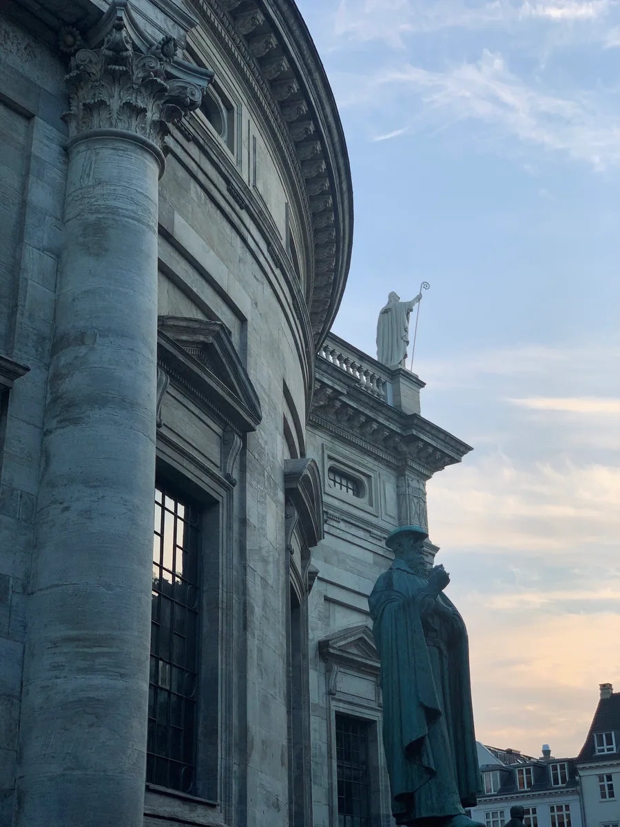 The curved stone façade of a church with a statue beside its columns