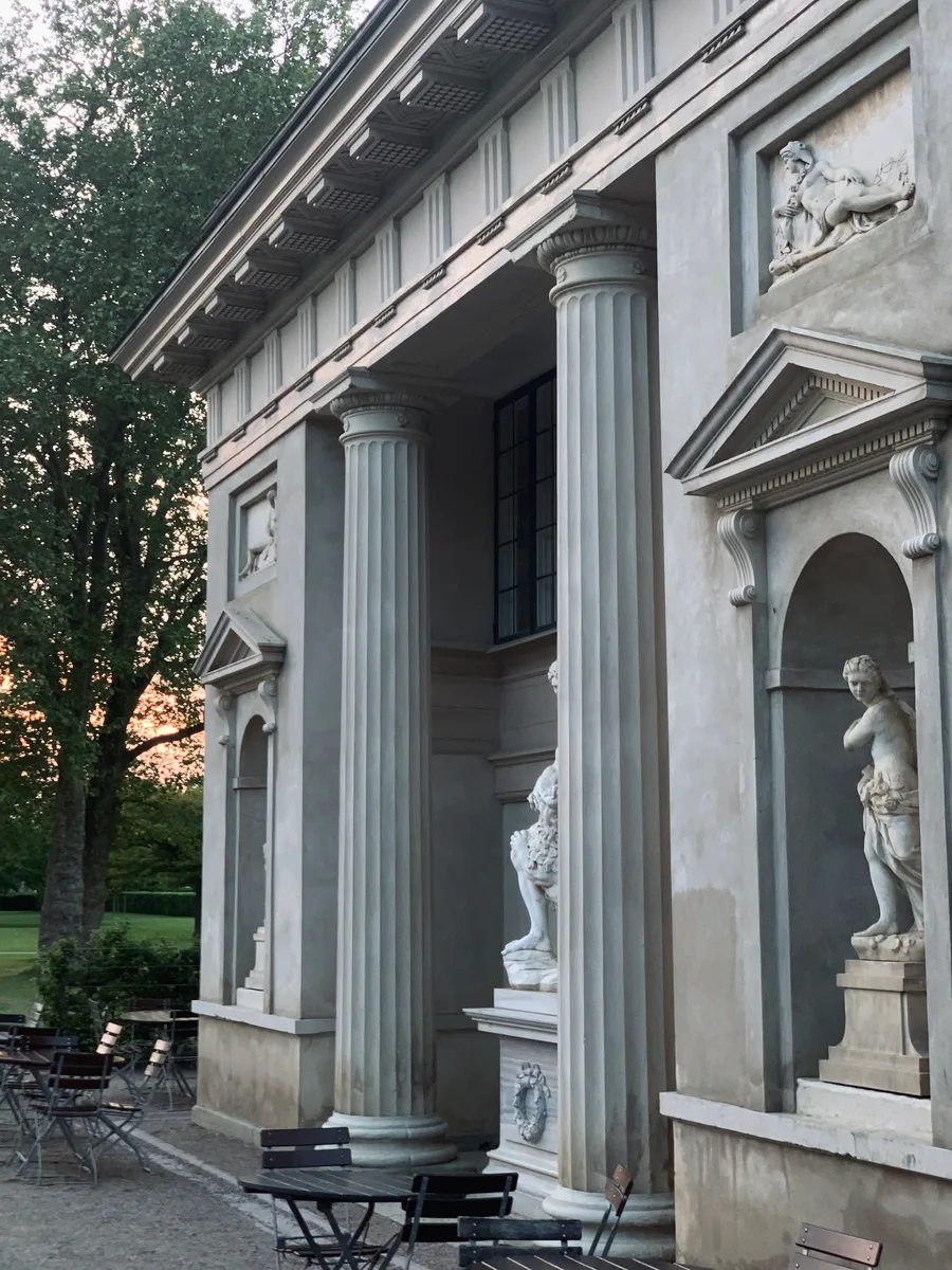 A stone colonnade with café tables in evening light