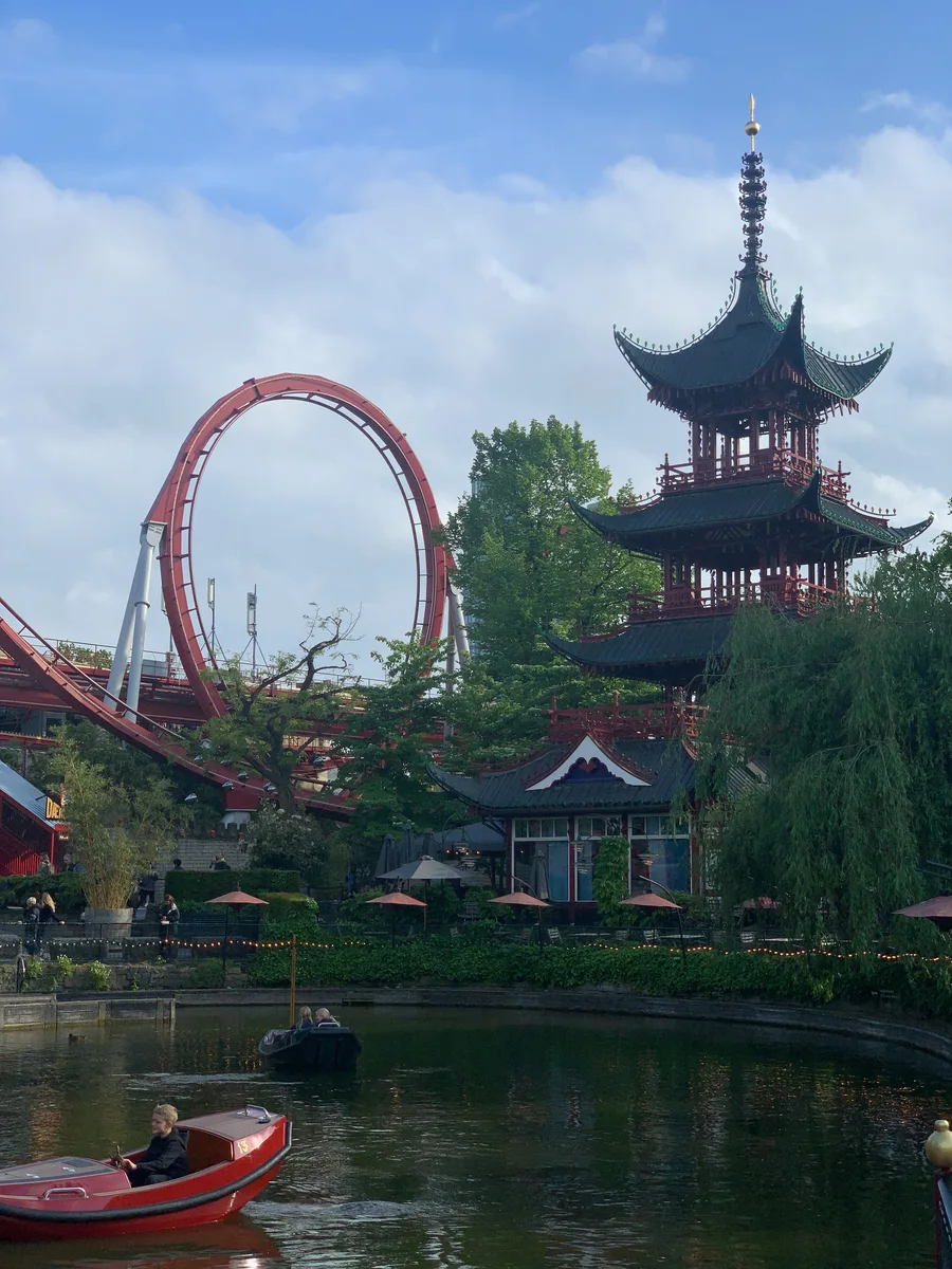 A pagoda beside a lake with a roller coaster loop beyond