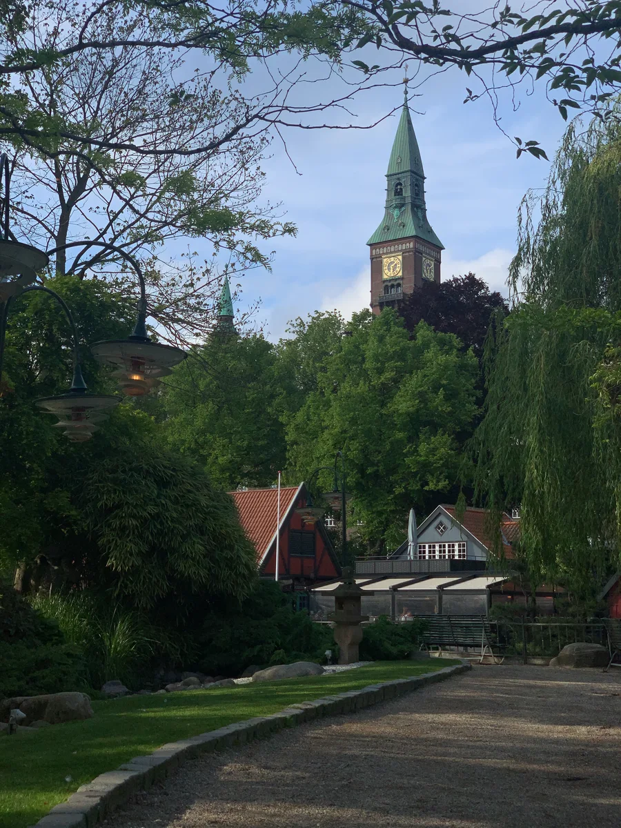 A garden path beneath trees with a tower in the distance