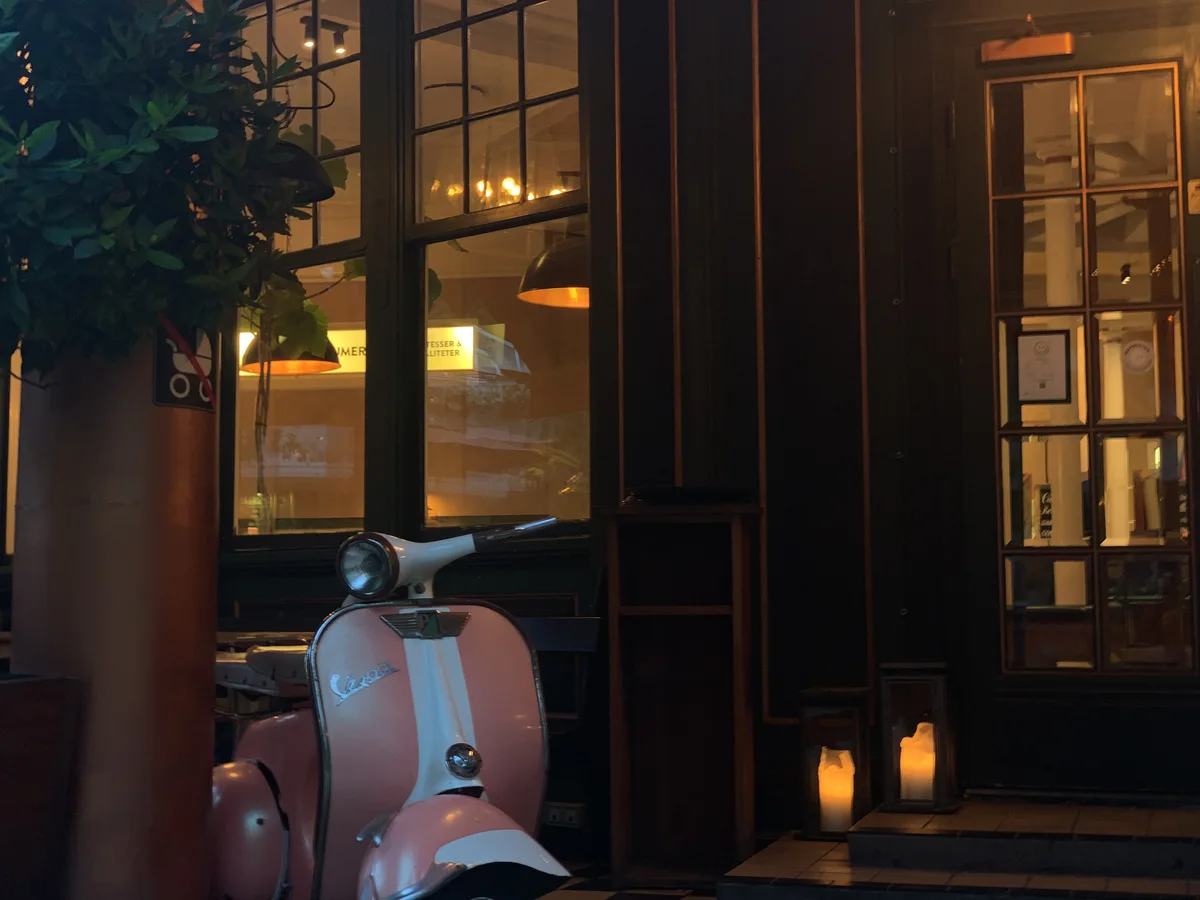 A pink scooter beside glowing restaurant windows