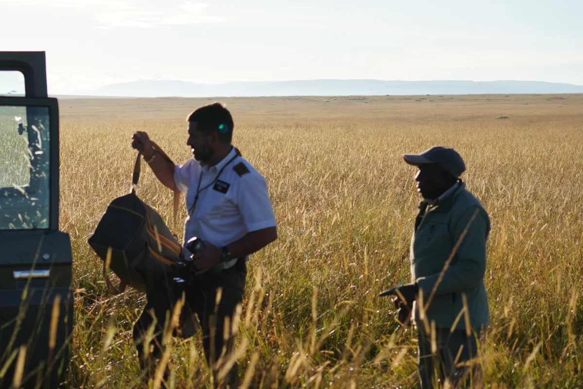 A pilot and driver standing beside a safari vehicle in tall grass