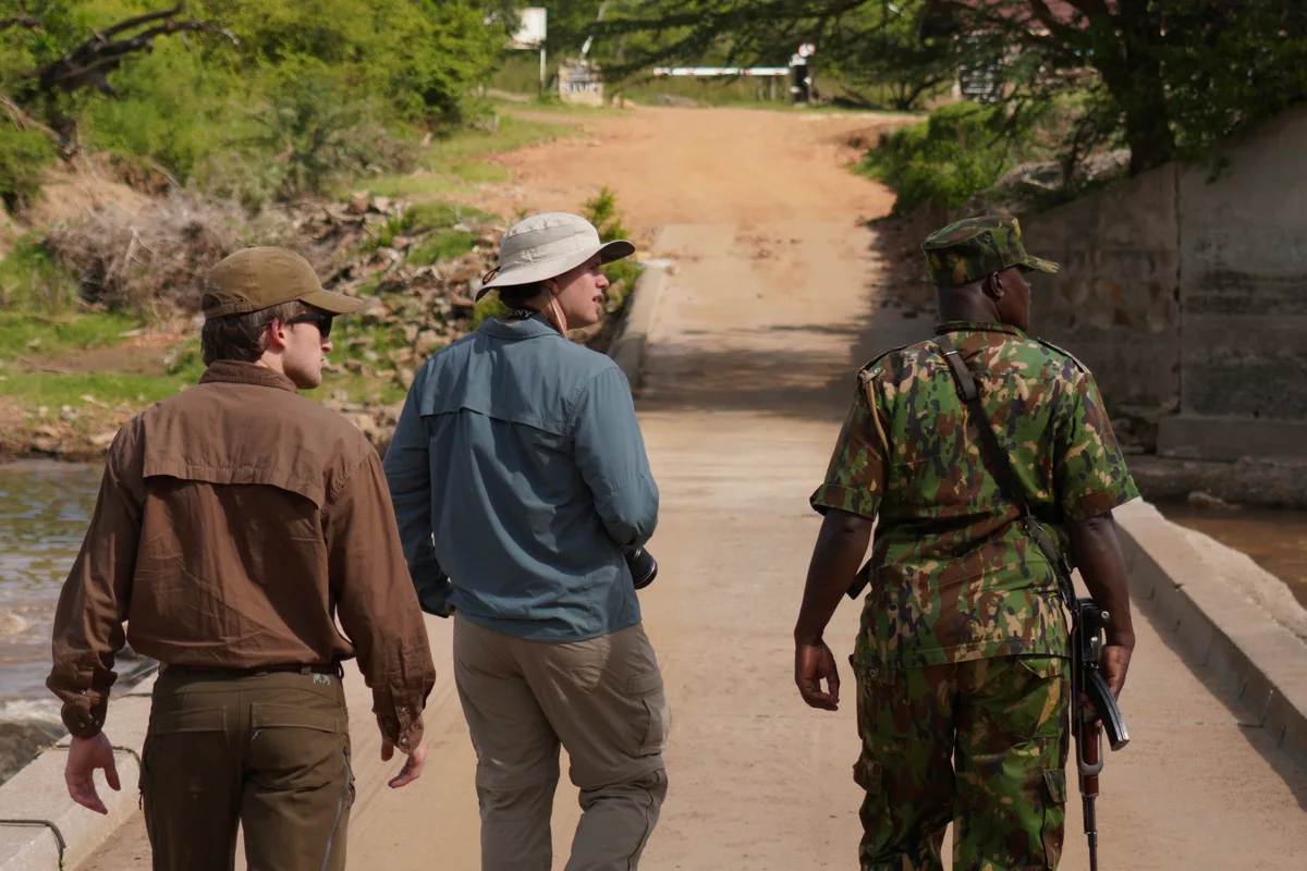 Two men and a soldier walking across a small dam