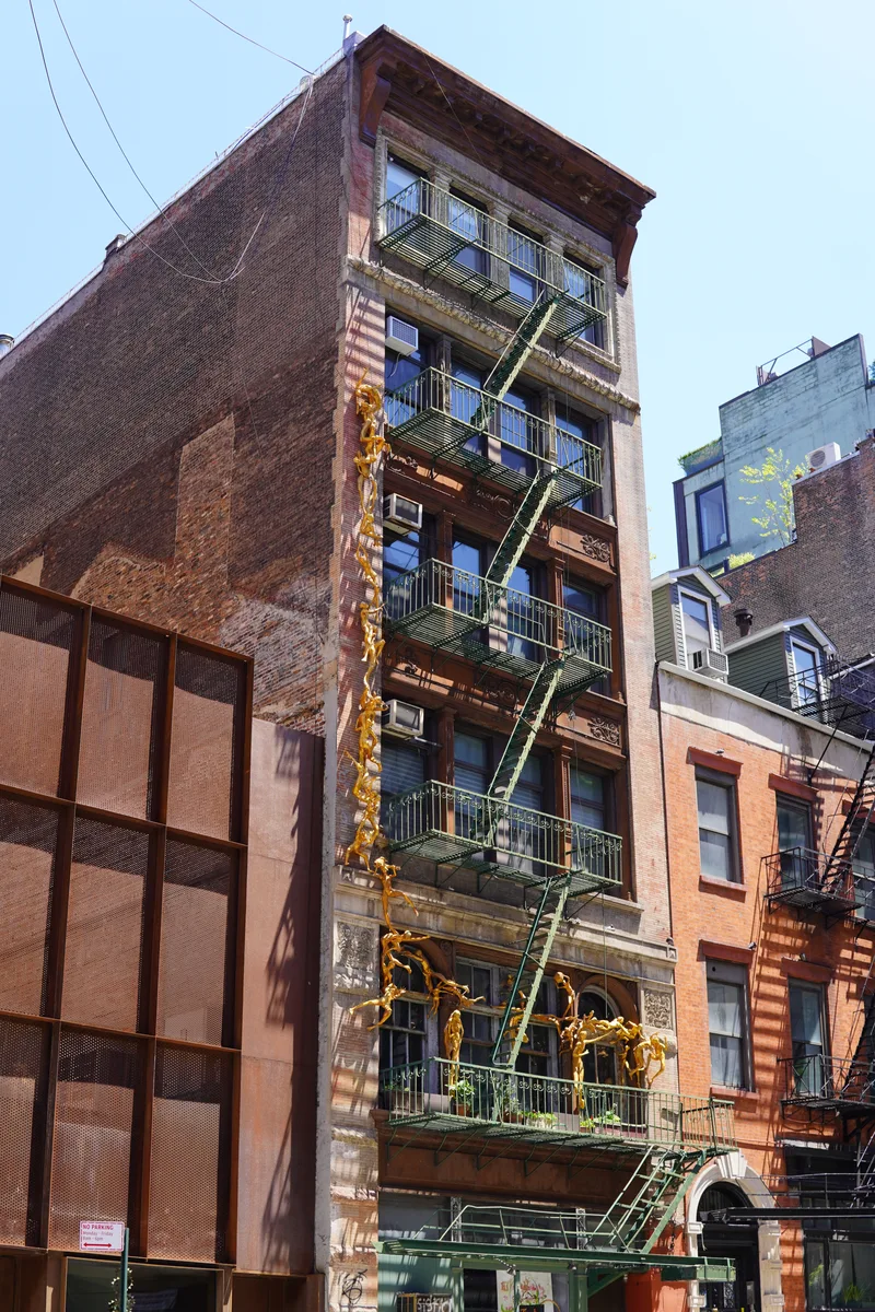 A historic brick building with green fire escapes and gold sculptures along the façade